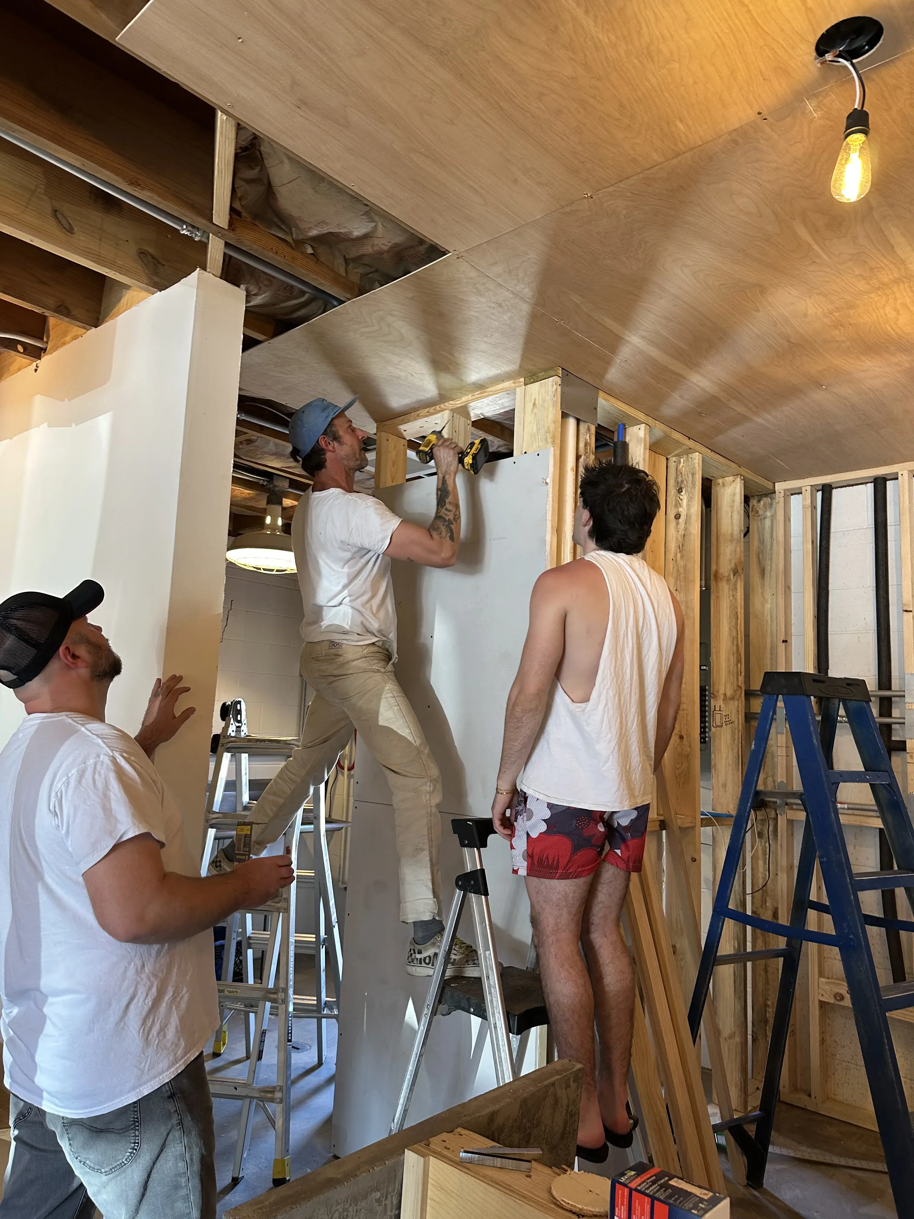 Moon Wolf crew working on the build-out at 920 Custer Rd, Richardson TX, before opening day — one on a ladder drilling, two steadying drywall sheets