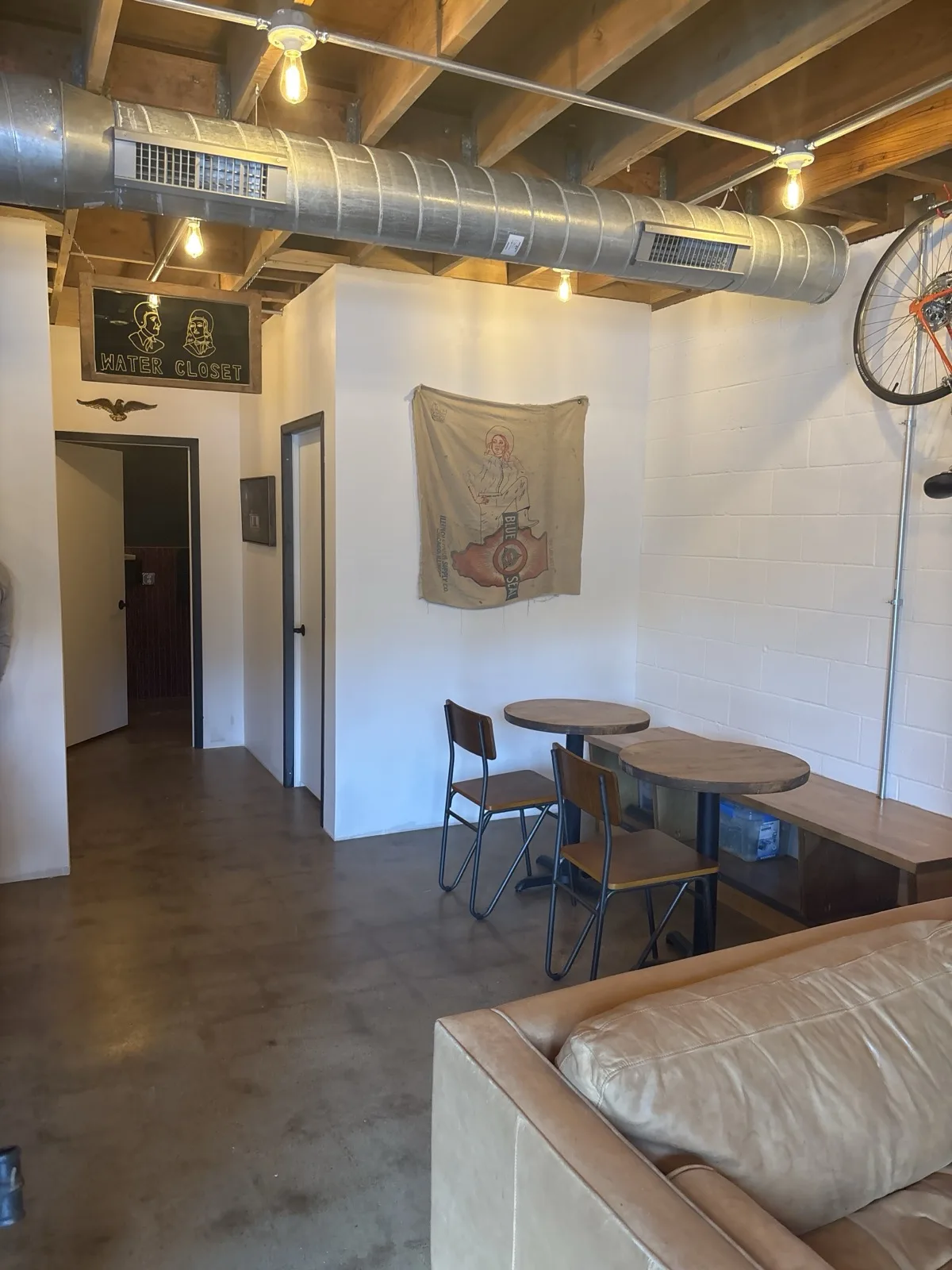 Seating area with Water Closet sign, exposed ductwork, and a vintage bike wheel on the wall